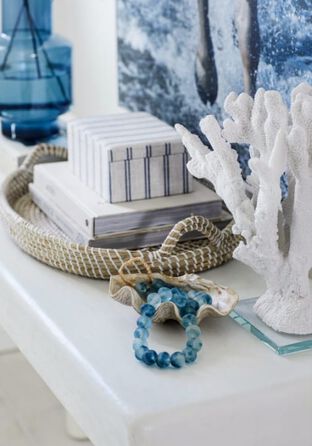 Detail shot showing beachy decor like blue seaglass beads and vase, a wicker tray, and white coral.